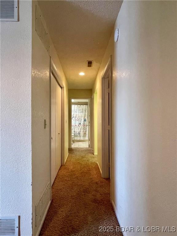 hallway featuring light colored carpet and a textured ceiling