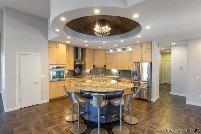 kitchen with wall chimney range hood, a raised ceiling, light brown cabinetry, and appliances with stainless steel finishes