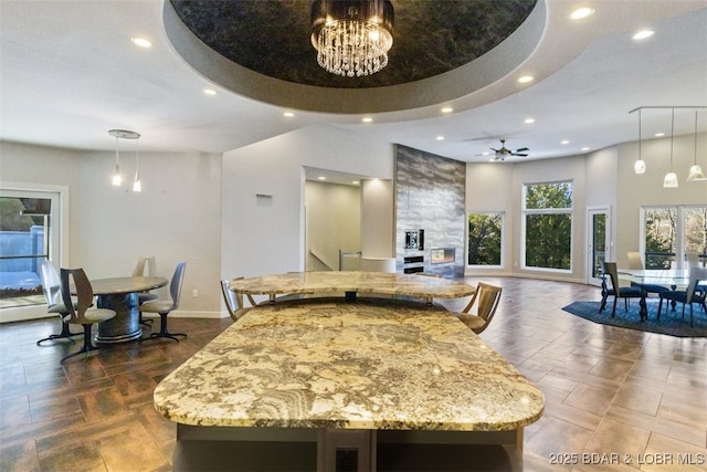 kitchen with a kitchen island, decorative light fixtures, ceiling fan with notable chandelier, light stone counters, and a tray ceiling