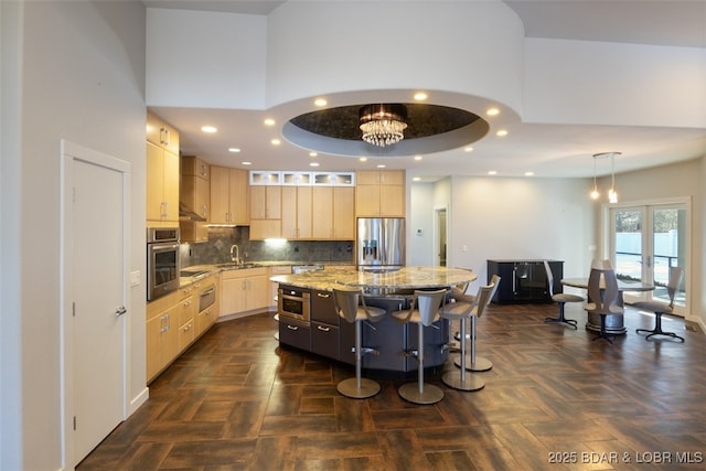 kitchen with light brown cabinets, appliances with stainless steel finishes, light stone countertops, a kitchen island, and dark parquet floors