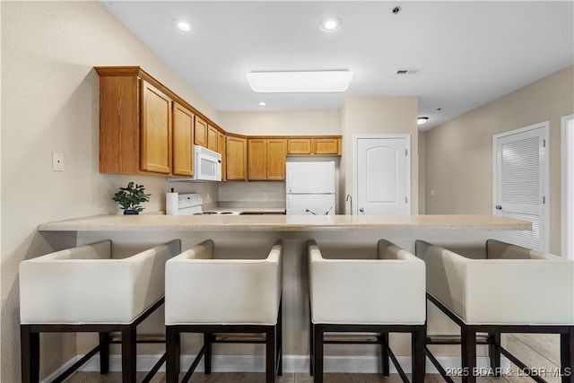 kitchen with white appliances, kitchen peninsula, and a breakfast bar