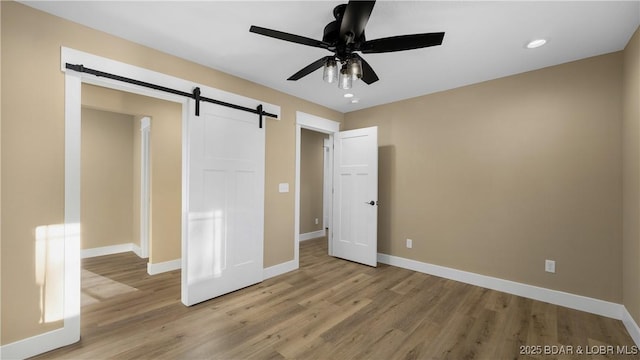 unfurnished bedroom with light wood-type flooring, ceiling fan, and a barn door