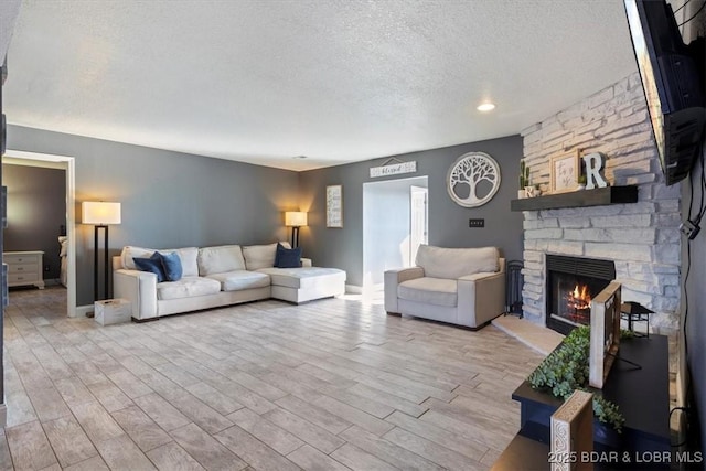 living room with light wood-type flooring, a textured ceiling, and a stone fireplace