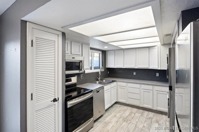 kitchen featuring light hardwood / wood-style flooring, sink, backsplash, white cabinetry, and stainless steel appliances