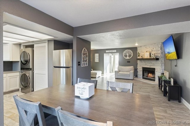 dining room featuring a fireplace, light hardwood / wood-style floors, a textured ceiling, and stacked washer and clothes dryer