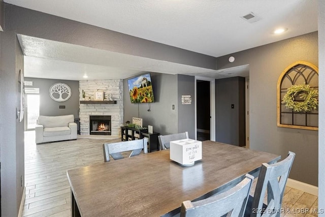 dining room with light wood-type flooring, a stone fireplace, and a textured ceiling