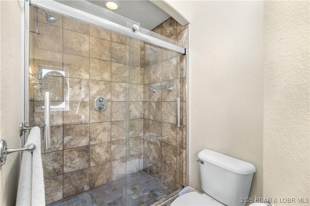 bathroom featuring a shower with door and toilet