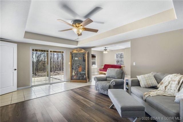 living room with hardwood / wood-style flooring, a raised ceiling, and ceiling fan