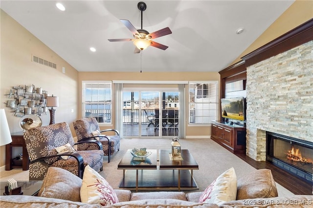 living room with ceiling fan, a stone fireplace, and vaulted ceiling