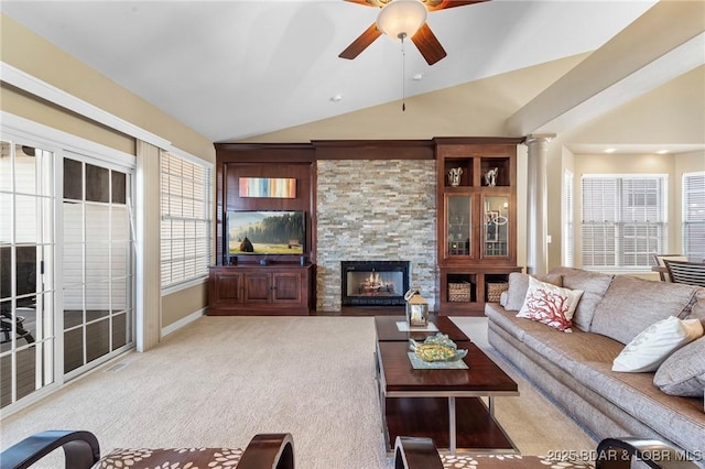 living room featuring vaulted ceiling, ceiling fan, light colored carpet, a stone fireplace, and decorative columns