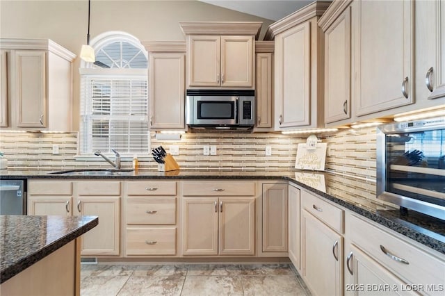 kitchen featuring stainless steel appliances, dark stone counters, tasteful backsplash, sink, and hanging light fixtures