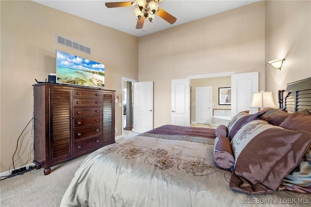 bedroom with ceiling fan, light colored carpet, ensuite bathroom, and a towering ceiling