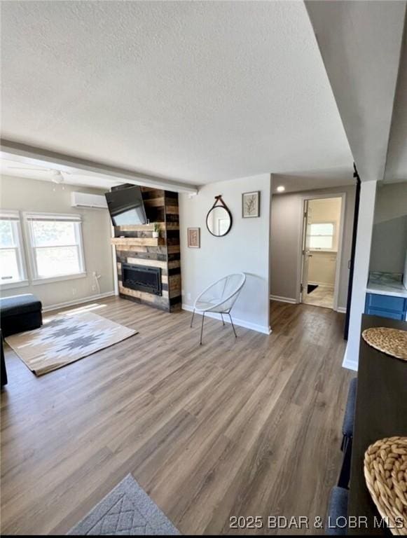 unfurnished living room featuring wood-type flooring, an AC wall unit, a textured ceiling, and a fireplace