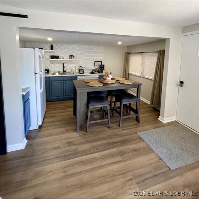 kitchen featuring white refrigerator, tasteful backsplash, sink, light wood-type flooring, and blue cabinets