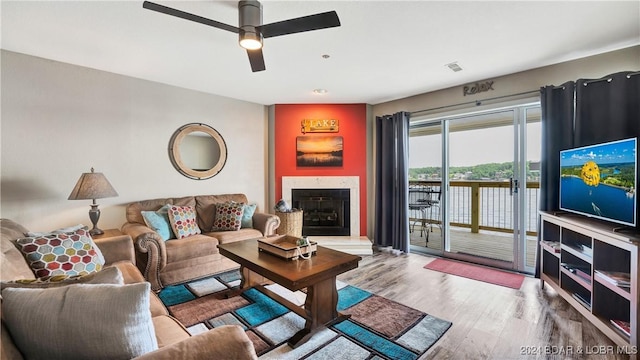 living room with wood-type flooring, a premium fireplace, and ceiling fan