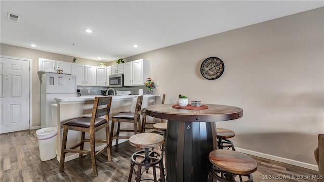 kitchen with tasteful backsplash, white cabinets, a kitchen breakfast bar, dark hardwood / wood-style flooring, and white refrigerator