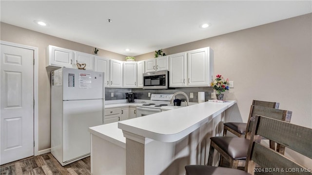 kitchen featuring dark wood-type flooring, a kitchen breakfast bar, kitchen peninsula, white appliances, and white cabinets