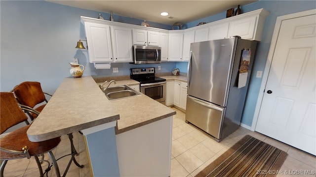 kitchen featuring sink, stainless steel appliances, white cabinets, a kitchen bar, and kitchen peninsula