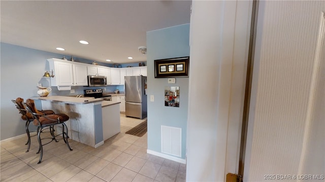 kitchen featuring a breakfast bar, stainless steel appliances, white cabinets, light tile patterned flooring, and kitchen peninsula