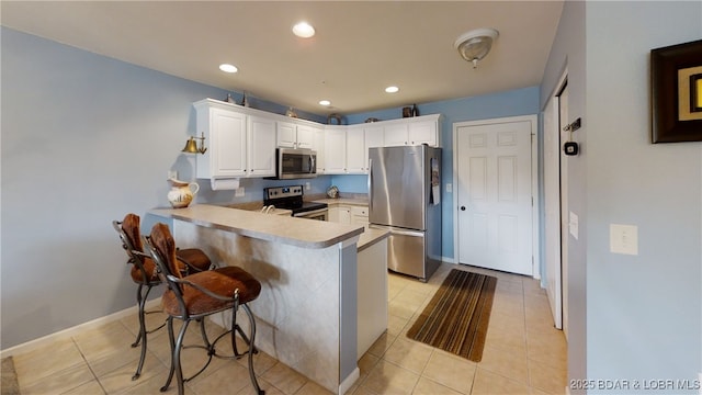 kitchen with a breakfast bar area, white cabinets, light tile patterned floors, kitchen peninsula, and stainless steel appliances