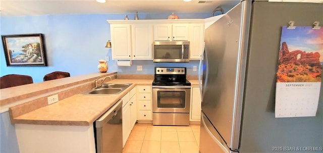 kitchen featuring sink, light tile patterned floors, appliances with stainless steel finishes, white cabinets, and kitchen peninsula