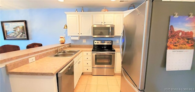 kitchen with appliances with stainless steel finishes, sink, white cabinets, light tile patterned floors, and kitchen peninsula