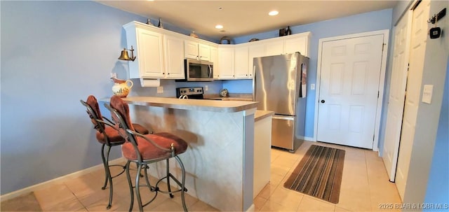 kitchen with white cabinetry, stainless steel appliances, a kitchen bar, and kitchen peninsula