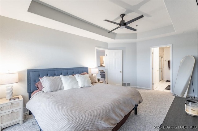 bedroom featuring ensuite bath, light colored carpet, ceiling fan, and a tray ceiling