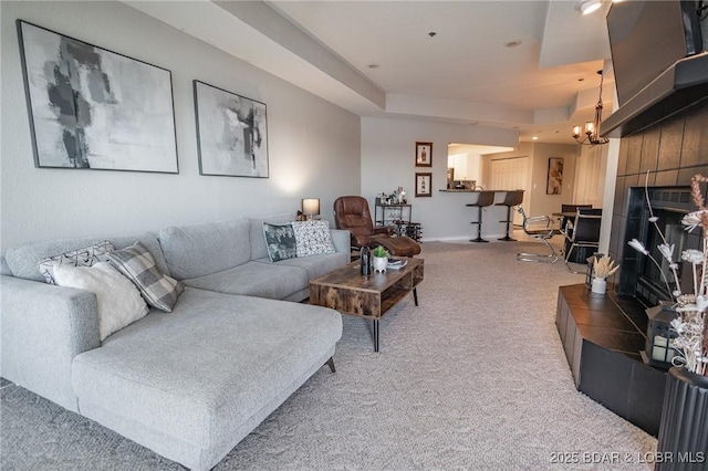 living room with an inviting chandelier, a tile fireplace, a raised ceiling, and carpet flooring