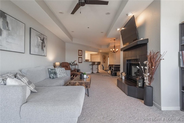 living room with a raised ceiling, a tile fireplace, carpet floors, and ceiling fan