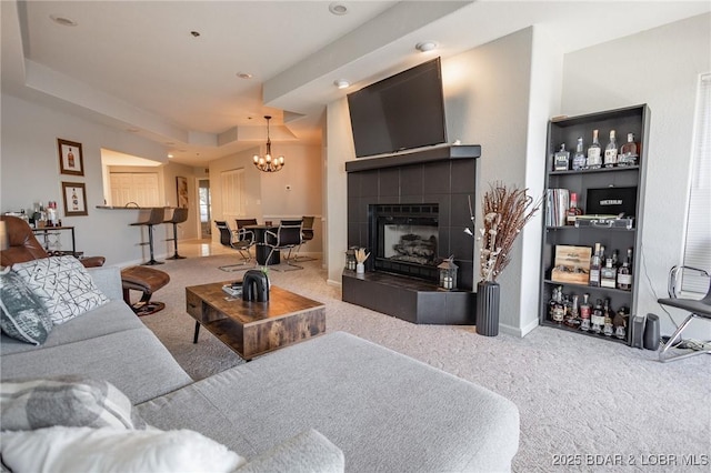 carpeted living room featuring a tiled fireplace, a notable chandelier, and a tray ceiling