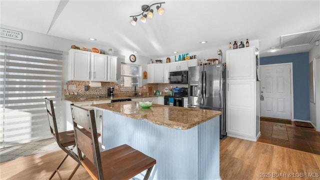 kitchen with light stone counters, black appliances, a center island, white cabinets, and backsplash