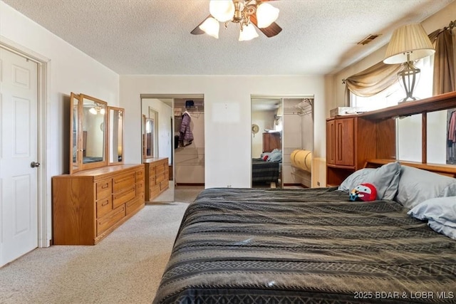 carpeted bedroom with a textured ceiling, ceiling fan, and two closets