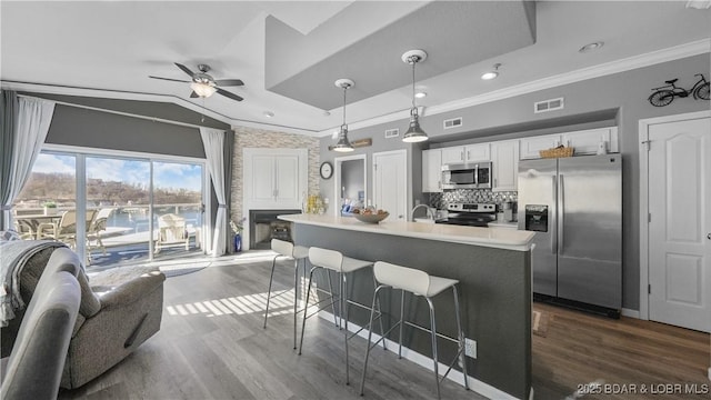 kitchen with appliances with stainless steel finishes, decorative light fixtures, white cabinetry, lofted ceiling, and a center island with sink