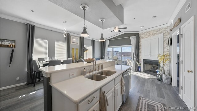 kitchen with sink, vaulted ceiling, stainless steel dishwasher, and a center island with sink