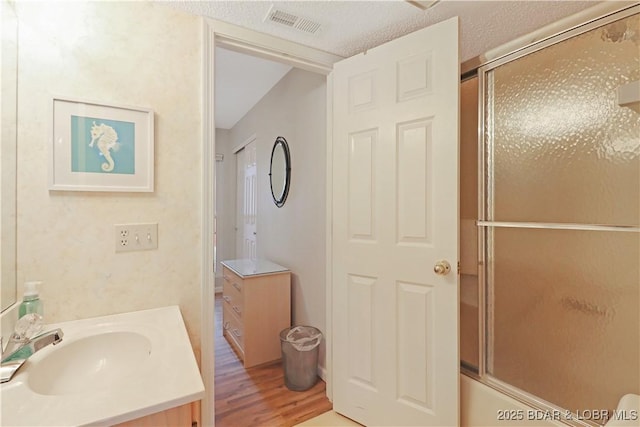 bathroom with wood-type flooring, combined bath / shower with glass door, vanity, and a textured ceiling