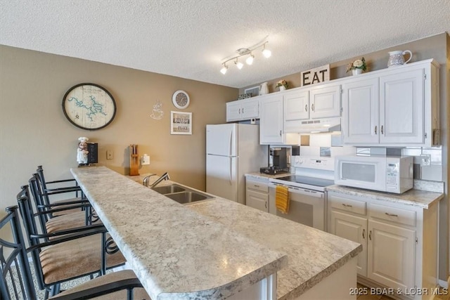 kitchen with sink, white appliances, a breakfast bar, a textured ceiling, and white cabinets