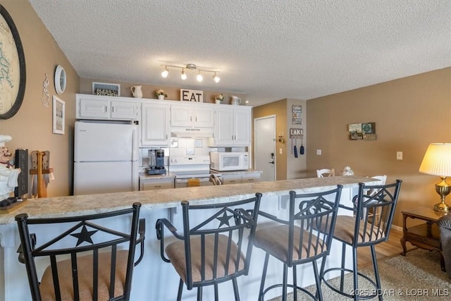 kitchen featuring white appliances, hardwood / wood-style flooring, a breakfast bar, white cabinetry, and a textured ceiling