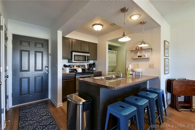 kitchen with dark brown cabinetry, a kitchen bar, a textured ceiling, kitchen peninsula, and stainless steel appliances