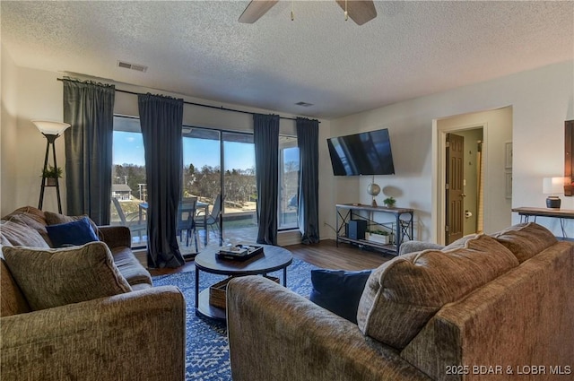 living room featuring dark hardwood / wood-style flooring, ceiling fan, and a textured ceiling