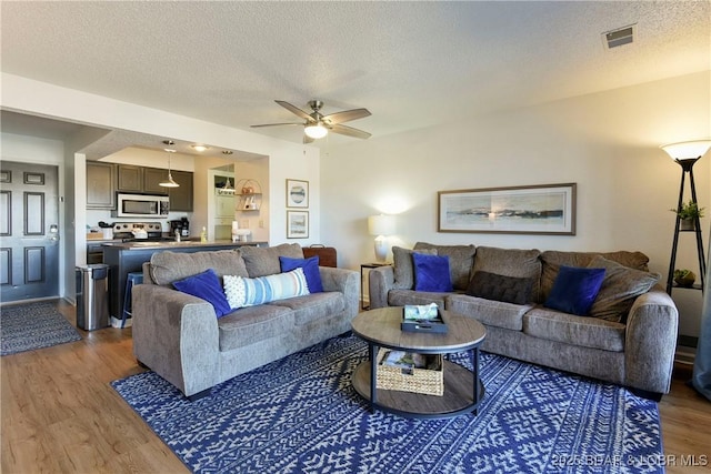 living room featuring ceiling fan, dark wood-type flooring, and a textured ceiling