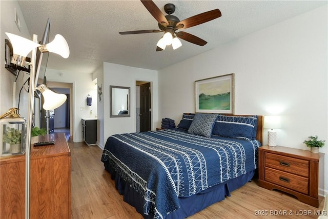 bedroom featuring ensuite bath, light hardwood / wood-style flooring, a textured ceiling, and ceiling fan