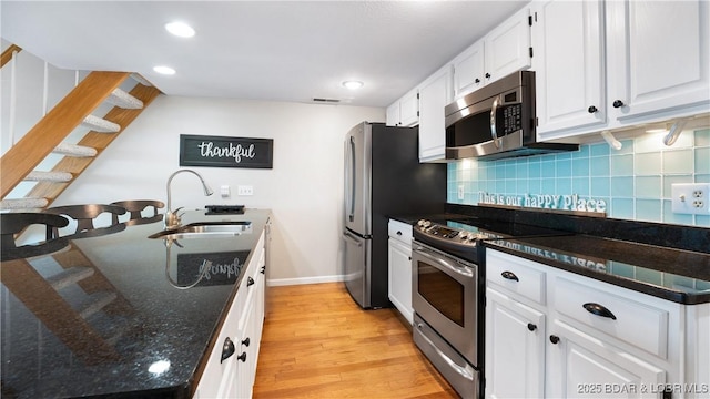 kitchen featuring sink, white cabinets, stainless steel appliances, light hardwood / wood-style floors, and backsplash