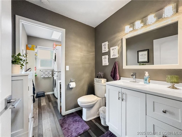 bathroom featuring stacked washer / dryer, toilet, wood-type flooring, and vanity