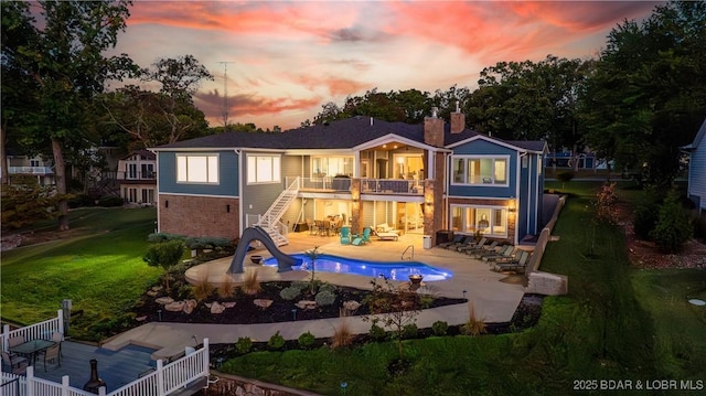 back house at dusk featuring a patio, a fenced in pool, and a balcony