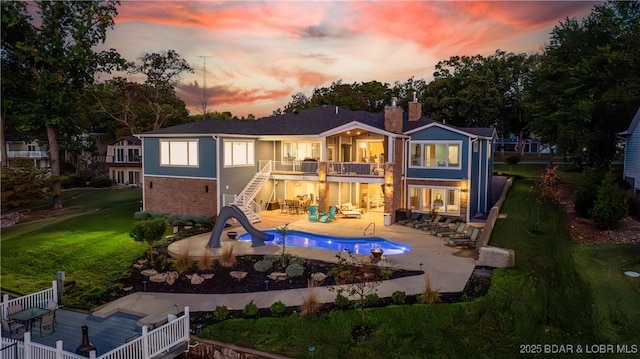 back of property at dusk featuring stairs, a chimney, a patio area, a balcony, and a yard