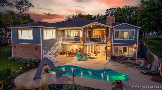 back house at dusk featuring a fenced in pool, a patio, and a balcony