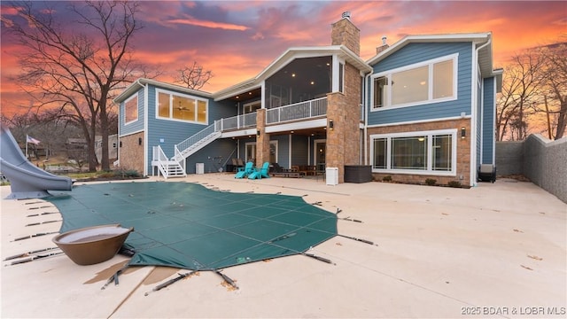 back house at dusk with a covered pool, a patio, and a sunroom