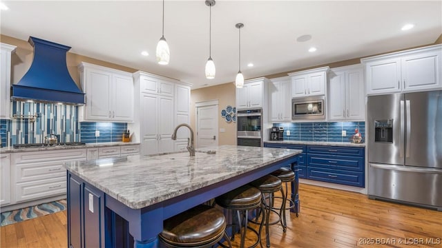 kitchen featuring blue cabinetry, appliances with stainless steel finishes, custom range hood, and a kitchen island with sink