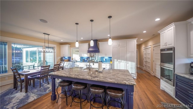 kitchen featuring custom exhaust hood, double oven, white cabinetry, and wood finished floors